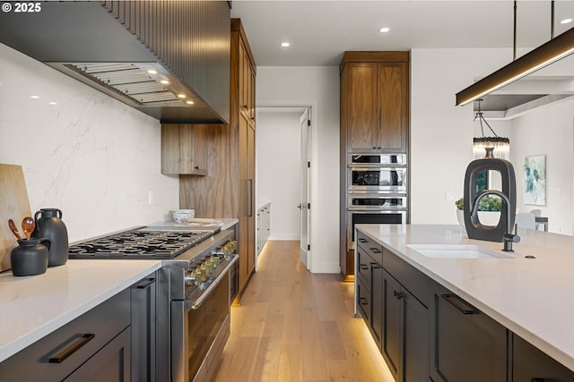 14410 Uplands Dr, Lake Oswego, OR 97034 - kitchen with appliances with stainless steel finishes, range hood, light wood finished floors, light stone countertops, and a sink