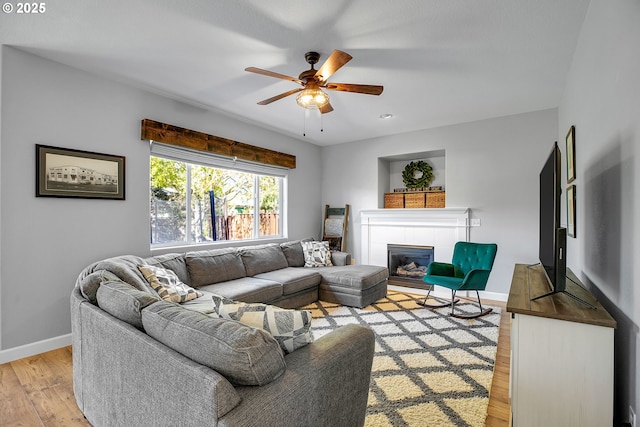 living area with a tiled fireplace, baseboards, ceiling fan, and light wood-type flooring