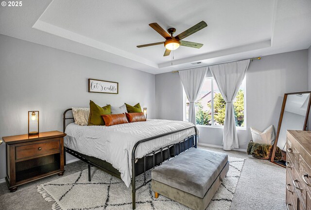 carpeted bedroom featuring baseboards, a ceiling fan, a tray ceiling, and visible vents