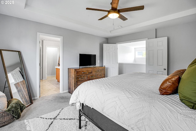 bedroom with light carpet, baseboards, a raised ceiling, a ceiling fan, and ensuite bath