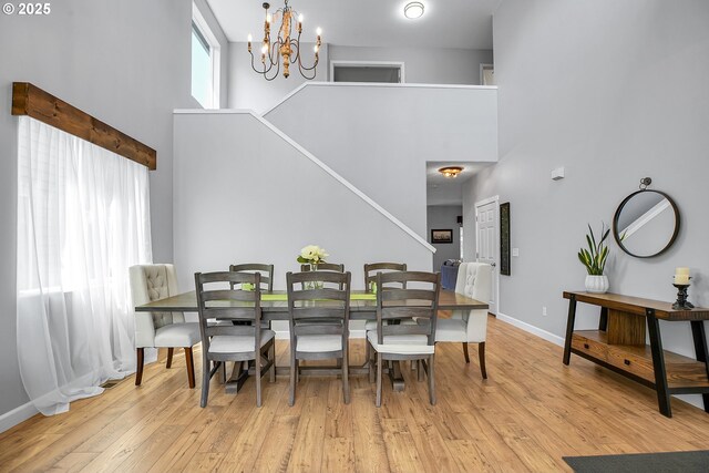dining space featuring stairway, a high ceiling, a chandelier, and light wood finished floors