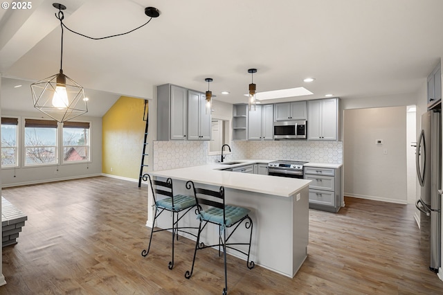 kitchen with a sink, a peninsula, gray cabinetry, and stainless steel appliances