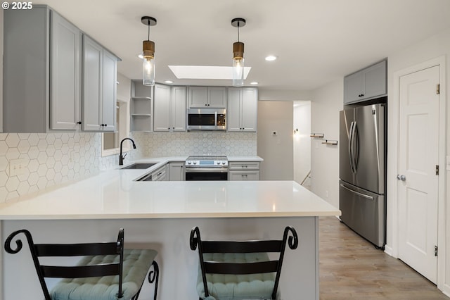 kitchen featuring gray cabinetry, a peninsula, a skylight, stainless steel appliances, and a sink