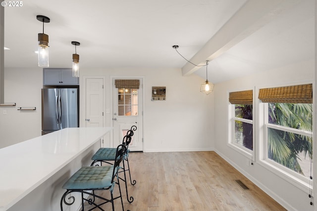 kitchen with a breakfast bar area, baseboards, light wood finished floors, vaulted ceiling with beams, and freestanding refrigerator