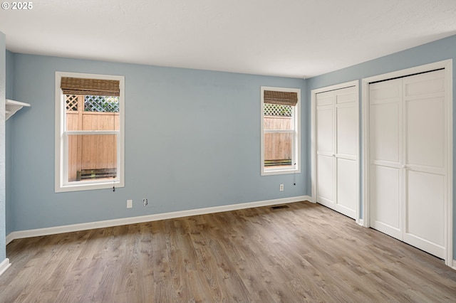 unfurnished bedroom featuring visible vents, baseboards, two closets, and wood finished floors