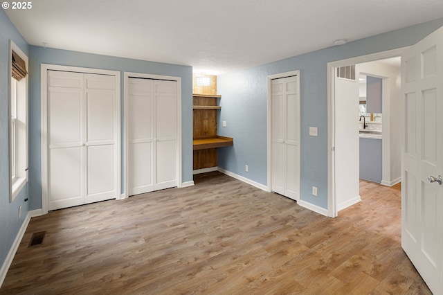 unfurnished bedroom with a sink, visible vents, two closets, and wood finished floors