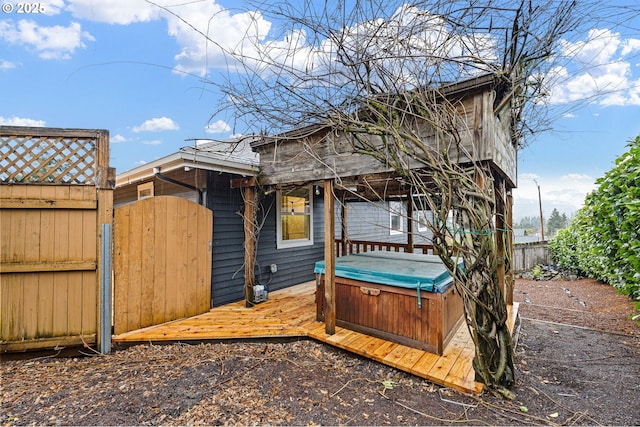 view of side of home with a gate, a hot tub, a deck, and fence