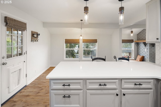 kitchen with light wood finished floors, a peninsula, light countertops, and lofted ceiling with beams