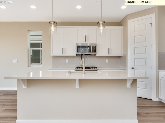 kitchen with a kitchen island with sink, pendant lighting, light hardwood / wood-style floors, and white cabinetry