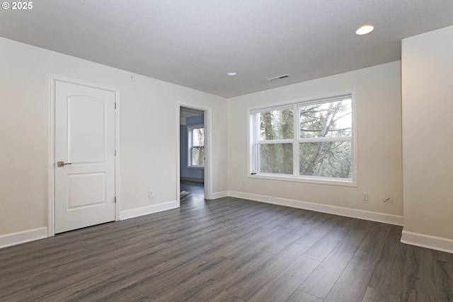 unfurnished room with baseboards, visible vents, dark wood-type flooring, and recessed lighting