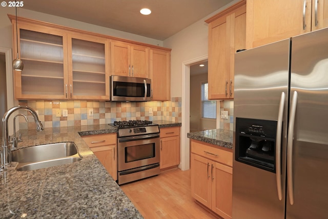 kitchen with appliances with stainless steel finishes, a sink, light wood-style floors, light brown cabinets, and backsplash