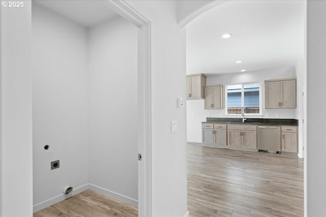 laundry area featuring light wood finished floors, hookup for an electric dryer, laundry area, arched walkways, and a sink