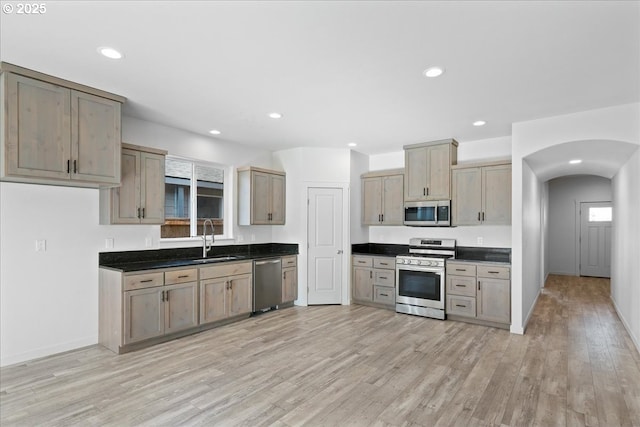 kitchen featuring dark countertops, light wood-type flooring, arched walkways, stainless steel appliances, and a sink