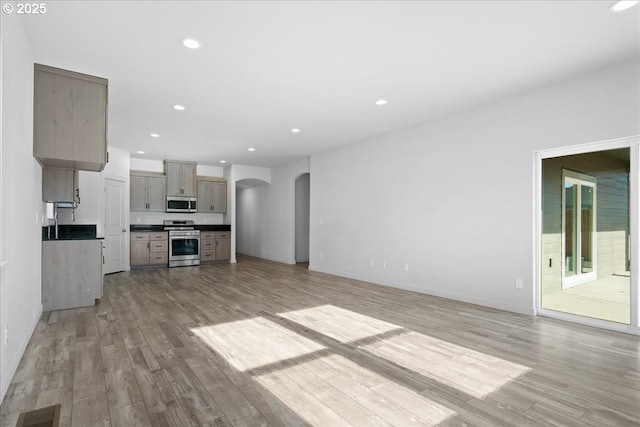 unfurnished living room with light wood-style flooring, recessed lighting, visible vents, and arched walkways