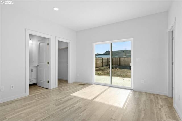 unfurnished bedroom with baseboards, a walk in closet, light wood-style floors, and access to outside