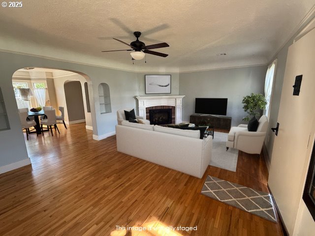 351 Juniper St, Junction City, OR 97448 - living room with wood finished floors, a fireplace, a textured ceiling, ceiling fan, and arched walkways