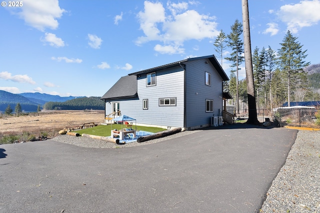 view of front of home featuring central AC unit, aphalt driveway, fence, a mountain view, and a front lawn