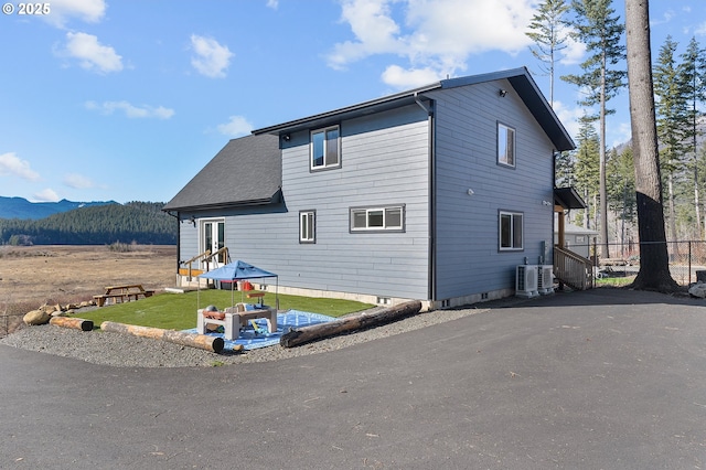 exterior space with a shingled roof, a front yard, cooling unit, and a mountain view