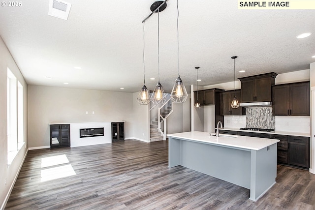 kitchen with dark brown cabinetry, sink, hanging light fixtures, a center island with sink, and decorative backsplash