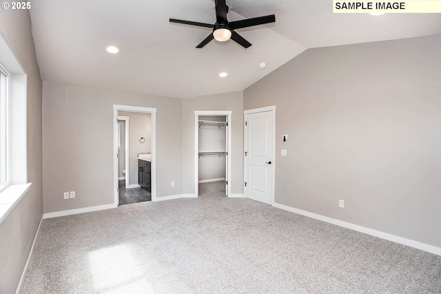 unfurnished bedroom featuring lofted ceiling, ensuite bathroom, dark colored carpet, a spacious closet, and a closet