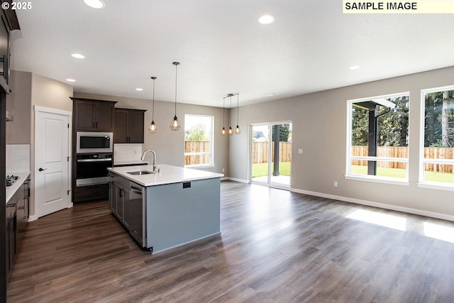 kitchen with dark brown cabinetry, sink, decorative light fixtures, appliances with stainless steel finishes, and an island with sink