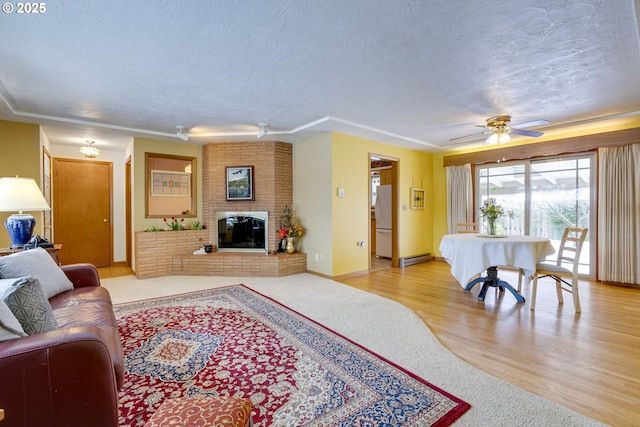 living room featuring ceiling fan, a baseboard heating unit, light hardwood / wood-style floors, a textured ceiling, and a brick fireplace