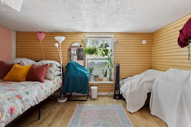 bedroom featuring a textured ceiling, light wood-style flooring, and wooden walls