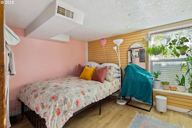 bedroom featuring a textured ceiling, wood walls, light wood-type flooring, and visible vents