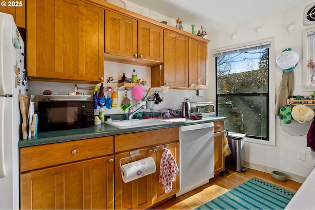 kitchen with brown cabinets, dark countertops, stainless steel dishwasher, a sink, and black microwave