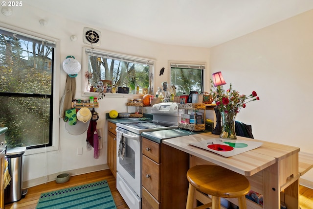 kitchen with white electric range, light wood-style floors, visible vents, and brown cabinets