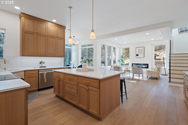 kitchen featuring light countertops, stainless steel dishwasher, decorative backsplash, light wood finished floors, and a glass covered fireplace