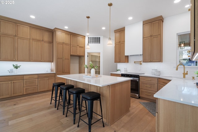 kitchen featuring a kitchen island, a sink, visible vents, stainless steel electric range, and light wood finished floors