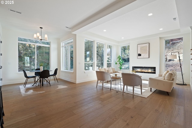 dining area with visible vents, a glass covered fireplace, a chandelier, light wood-type flooring, and baseboards