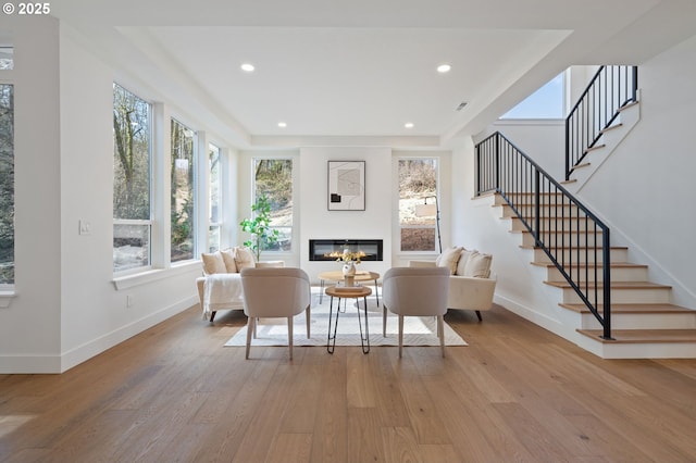 living area with a glass covered fireplace, baseboards, light wood finished floors, and recessed lighting