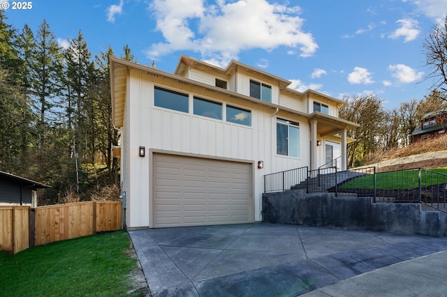 view of front of property featuring concrete driveway, an attached garage, board and batten siding, fence, and a front lawn