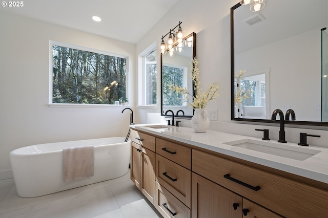 bathroom with double vanity, a freestanding tub, a sink, and visible vents