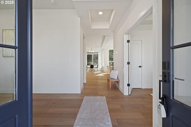 hall with baseboards, a chandelier, wood finished floors, and a raised ceiling