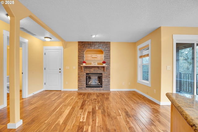 unfurnished living room featuring a stone fireplace, light wood finished floors, and a textured ceiling