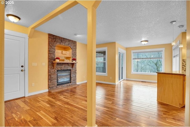 unfurnished living room with light wood-type flooring, baseboards, a stone fireplace, and a textured ceiling