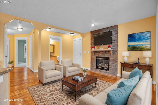 living room featuring visible vents, arched walkways, light wood-style flooring, a textured ceiling, and a stone fireplace