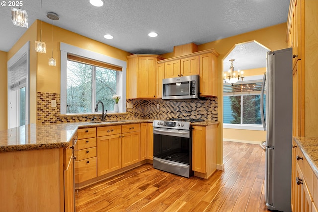 kitchen featuring arched walkways, light stone counters, stainless steel appliances, light wood-style floors, and a sink