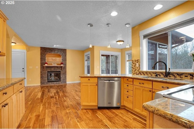 kitchen with a fireplace, a sink, backsplash, dishwasher, and light wood finished floors