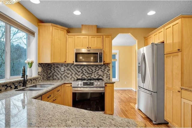 kitchen featuring light stone counters, stainless steel appliances, a sink, and light brown cabinetry