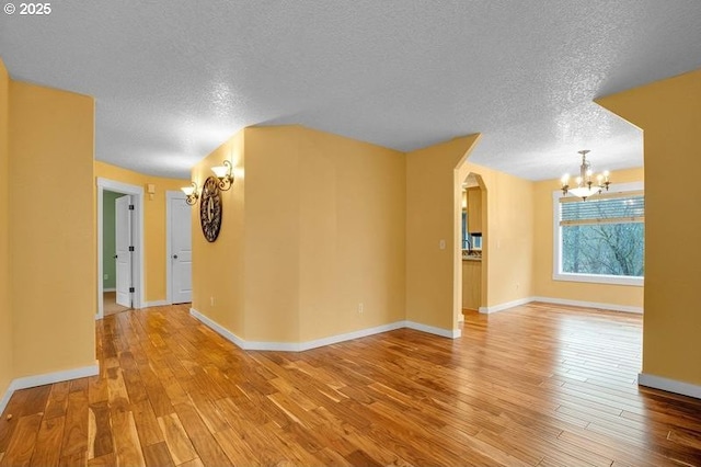 spare room with arched walkways, baseboards, light wood finished floors, and an inviting chandelier