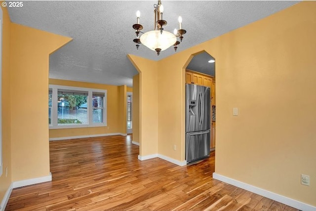 interior space featuring arched walkways, a textured ceiling, a notable chandelier, baseboards, and light wood finished floors