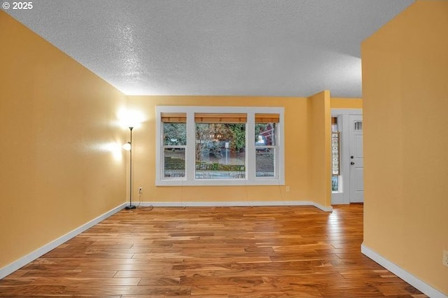 empty room with a textured ceiling, baseboards, and wood finished floors