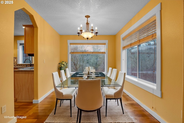 dining space with baseboards, a chandelier, arched walkways, and wood finished floors