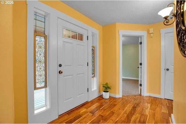 foyer with light wood finished floors, baseboards, a textured ceiling, and an inviting chandelier