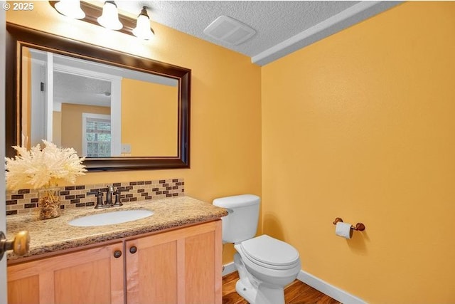 bathroom with visible vents, toilet, a textured ceiling, vanity, and backsplash