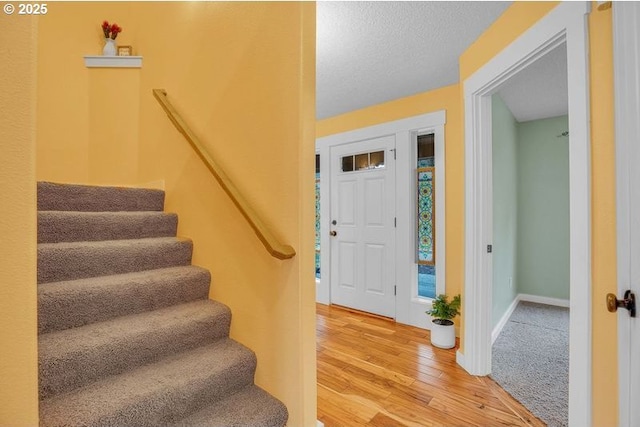 entrance foyer featuring stairs, a textured ceiling, wood finished floors, and baseboards